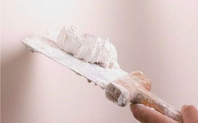 Người thợ đang dùng bay phết bột trét lên tường, chuẩn bị bề mặt cho công việc trang trí hoặc sơn.