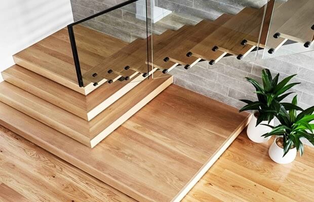 Cầu thang gỗ hiện đại kết hợp lan can kính, trang trí với cây xanh trong chậu trắng, tạo không gian nội thất sang trọng.