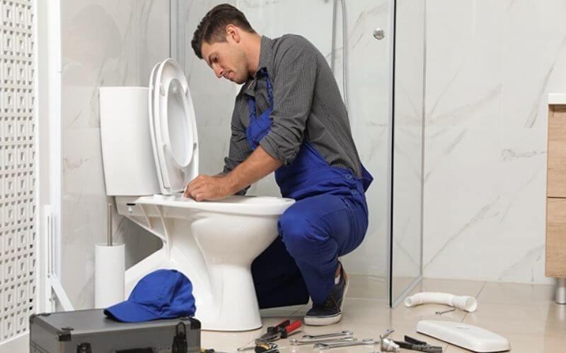 Kỹ thuật viên sửa chữa bồn cầu trong phòng tắm, dụng cụ nằm rải rác trên sàn.