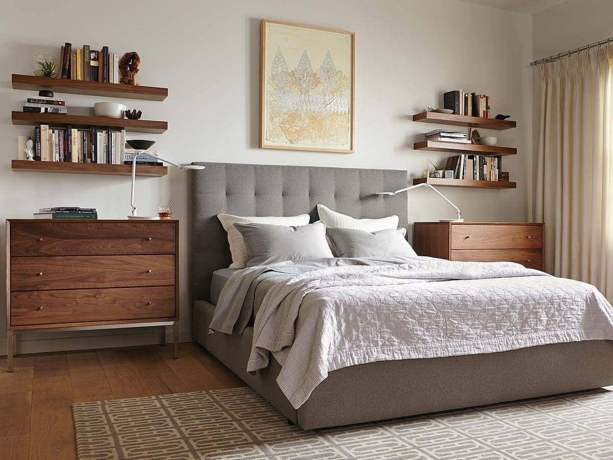 Phòng ngủ hiện đại với giường xám, tủ gỗ, và kệ sách treo tường, ánh sáng tự nhiên qua rèm cửa.