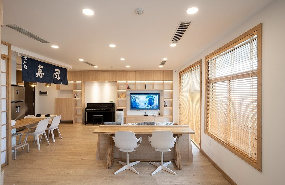 Phòng khách hiện đại với bàn gỗ, ghế xoay trắng, tivi treo tường và cửa sổ lớn.