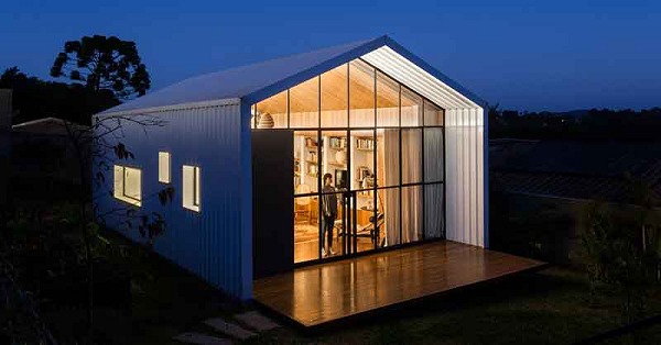 Ngôi nhà hiện đại vào buổi tối với ánh sáng ấm áp từ cửa kính lớn, ngoại thất màu trắng, kiến trúc tối giản.