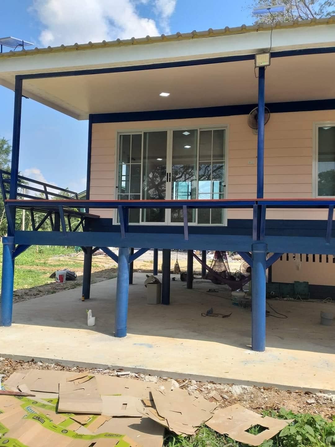 Nhà sàn hiện đại với khung màu xanh và cửa kính trượt, nằm giữa không gian xanh thiên nhiên.