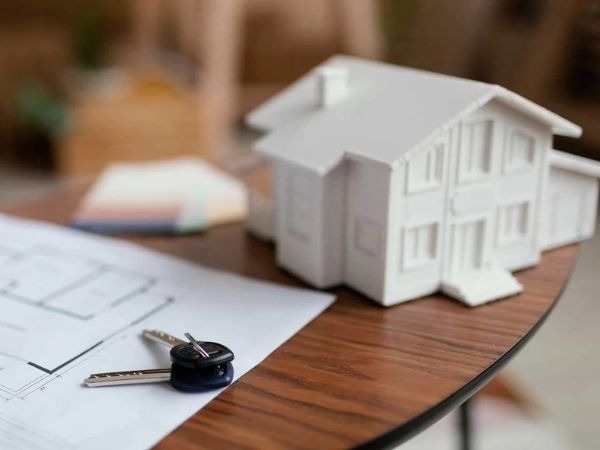 Mô hình nhà, bản vẽ thiết kế và chìa khóa trên bàn gỗ, tượng trưng cho việc mua và thiết kế nhà mới.