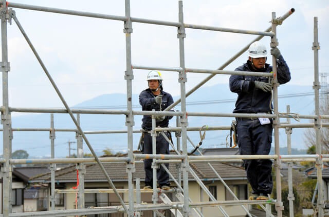 Công nhân xây dựng đang lắp đặt giàn giáo an toàn tại công trường, đội mũ bảo hộ và mặc đồng phục.