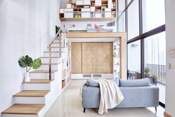 Phòng khách phong cách tối giản với gác lửng, cầu thang gỗ, và sofa xám nhạt cạnh cửa sổ lớn tràn ngập ánh sáng.