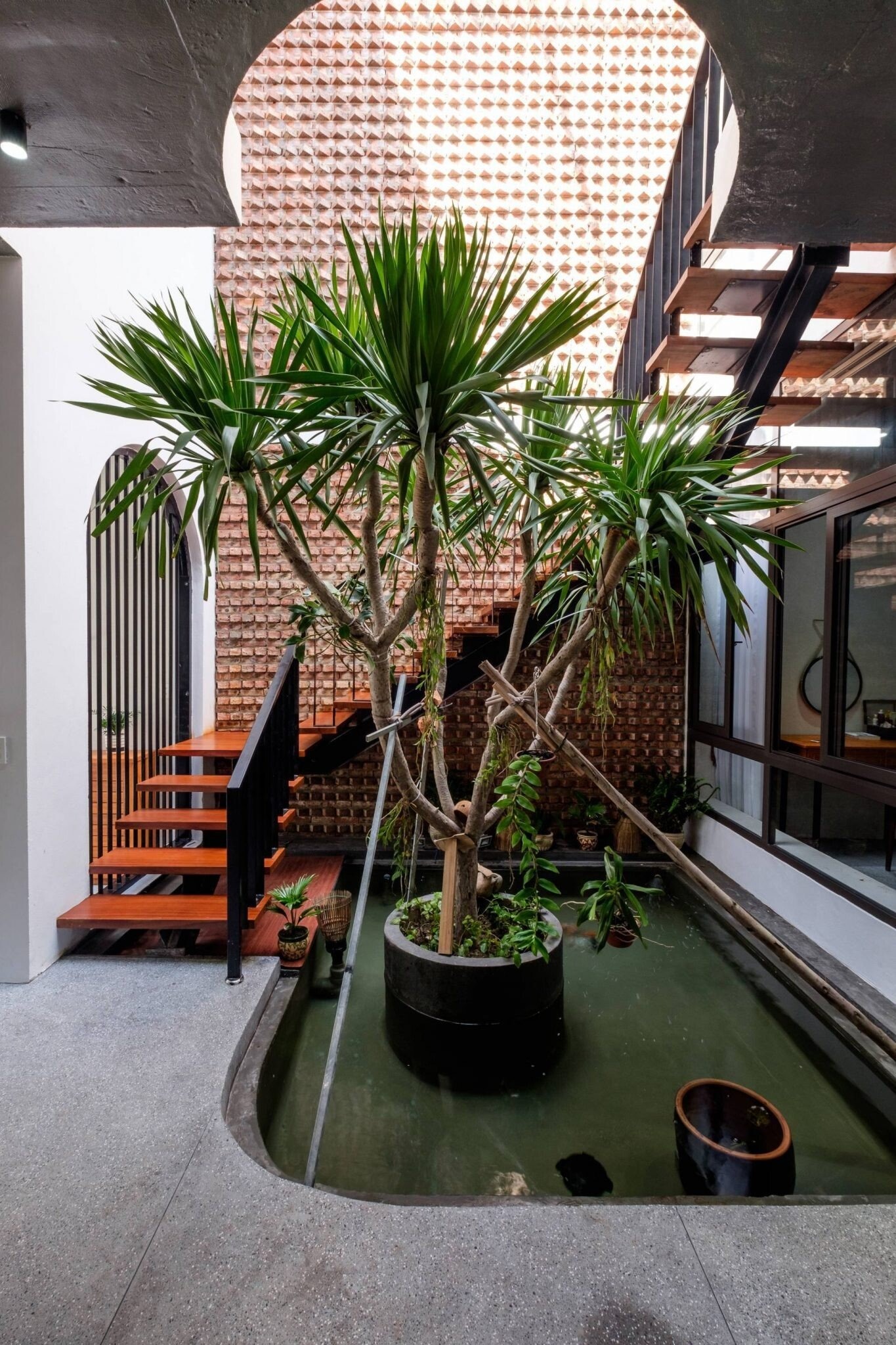 Cây xanh trong nhà với cầu thang gỗ và tường gạch; không gian sống xanh và thoáng đãng.