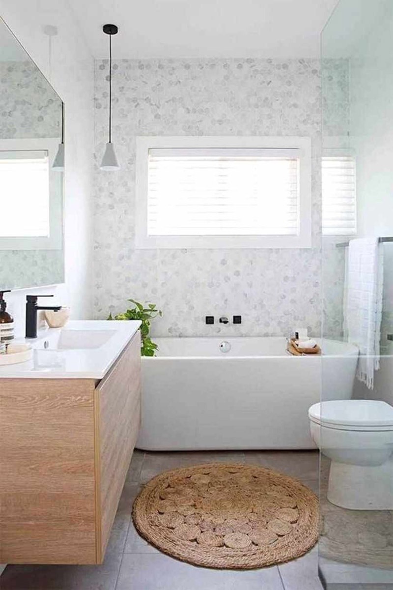 Phòng tắm hiện đại với bồn tắm trắng, tủ gỗ và thảm tròn, tạo không gian thư giãn và sáng sủa.