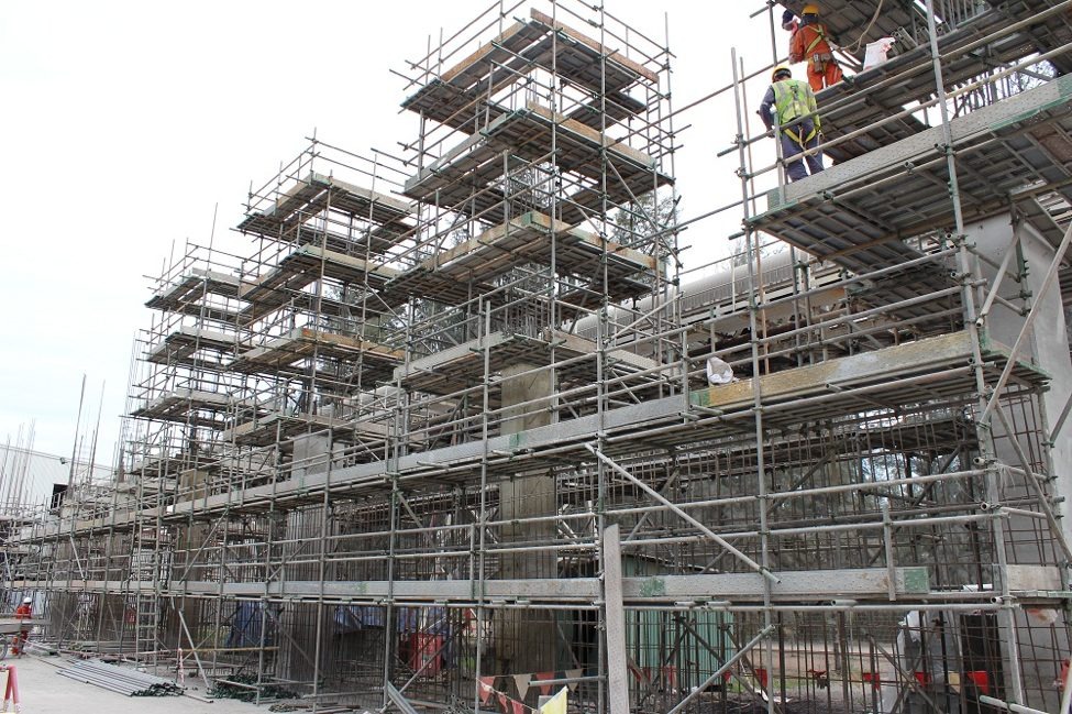 Giàn giáo công trình xây dựng với công nhân làm việc trên cao, nền trời trong.