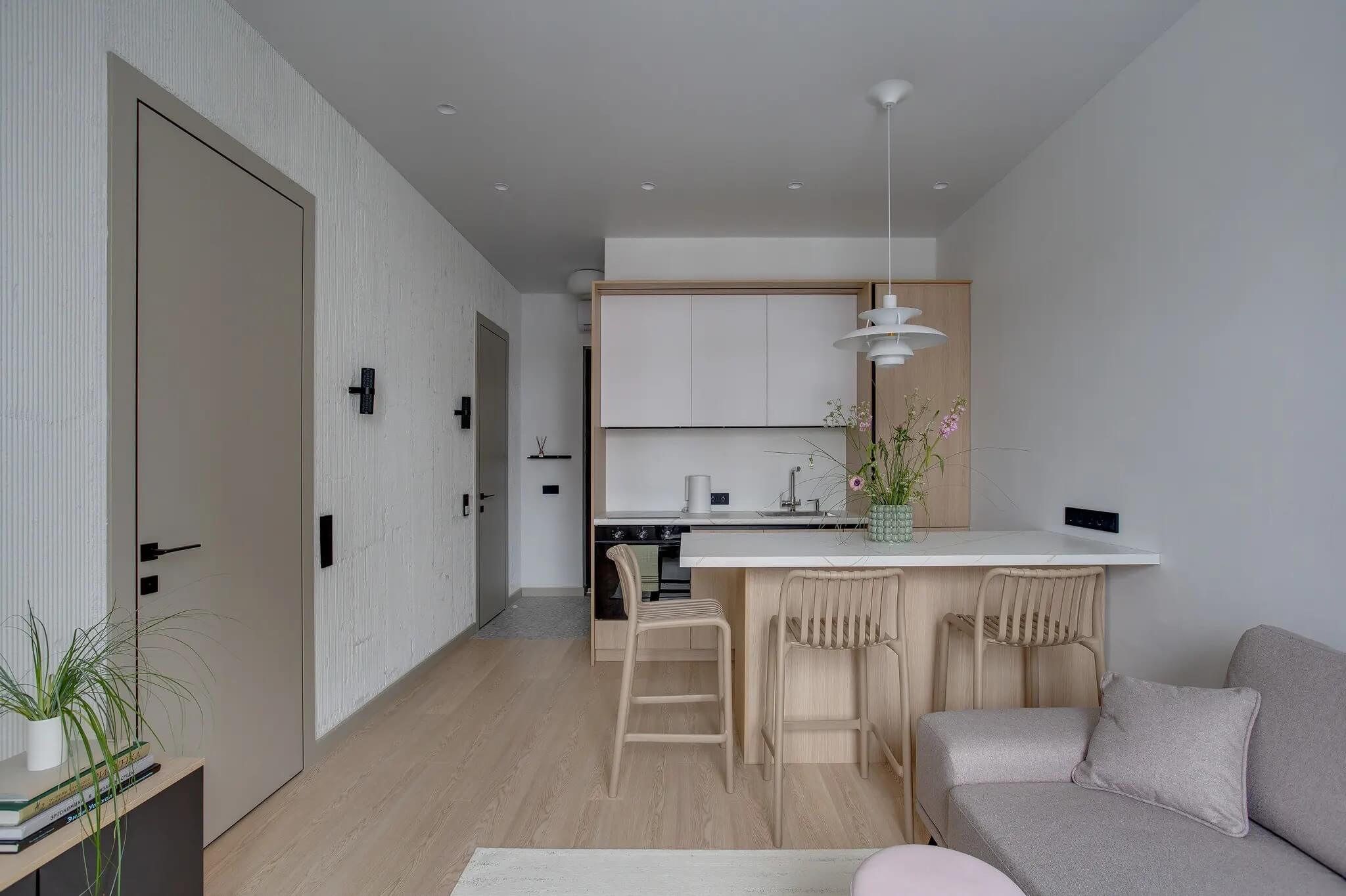 Căn hộ tối giản với bàn ăn nhỏ, ghế sofa xám và tủ bếp sáng màu, tạo không gian ấm cúng và hiện đại.