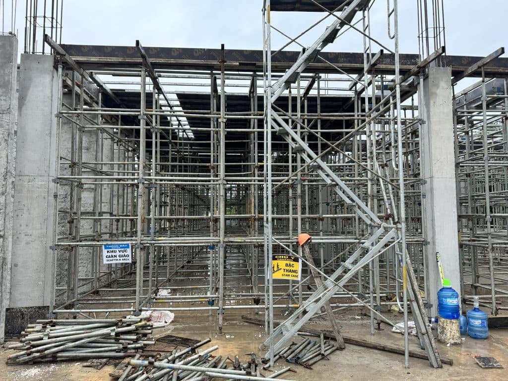 Giàn giáo và khu vực thi công xây dựng với nhiều ống thép và biển cảnh báo an toàn.
