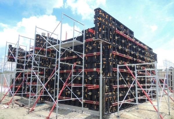 Giàn giáo xây dựng thi công tại công trường với mảng bê tông lớn, nền trời xanh và mây trắng.