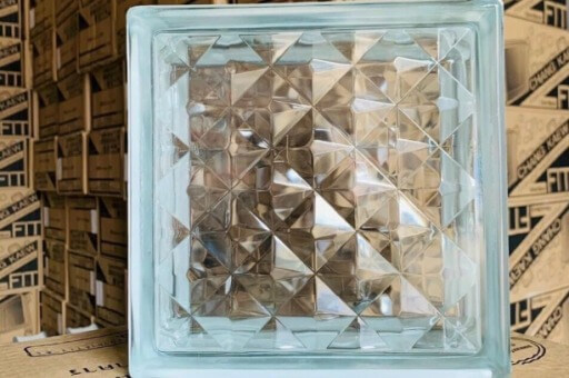 Khối kính họa tiết hình học, phản chiếu ánh sáng với nền các hộp giấy chồng lên nhau.