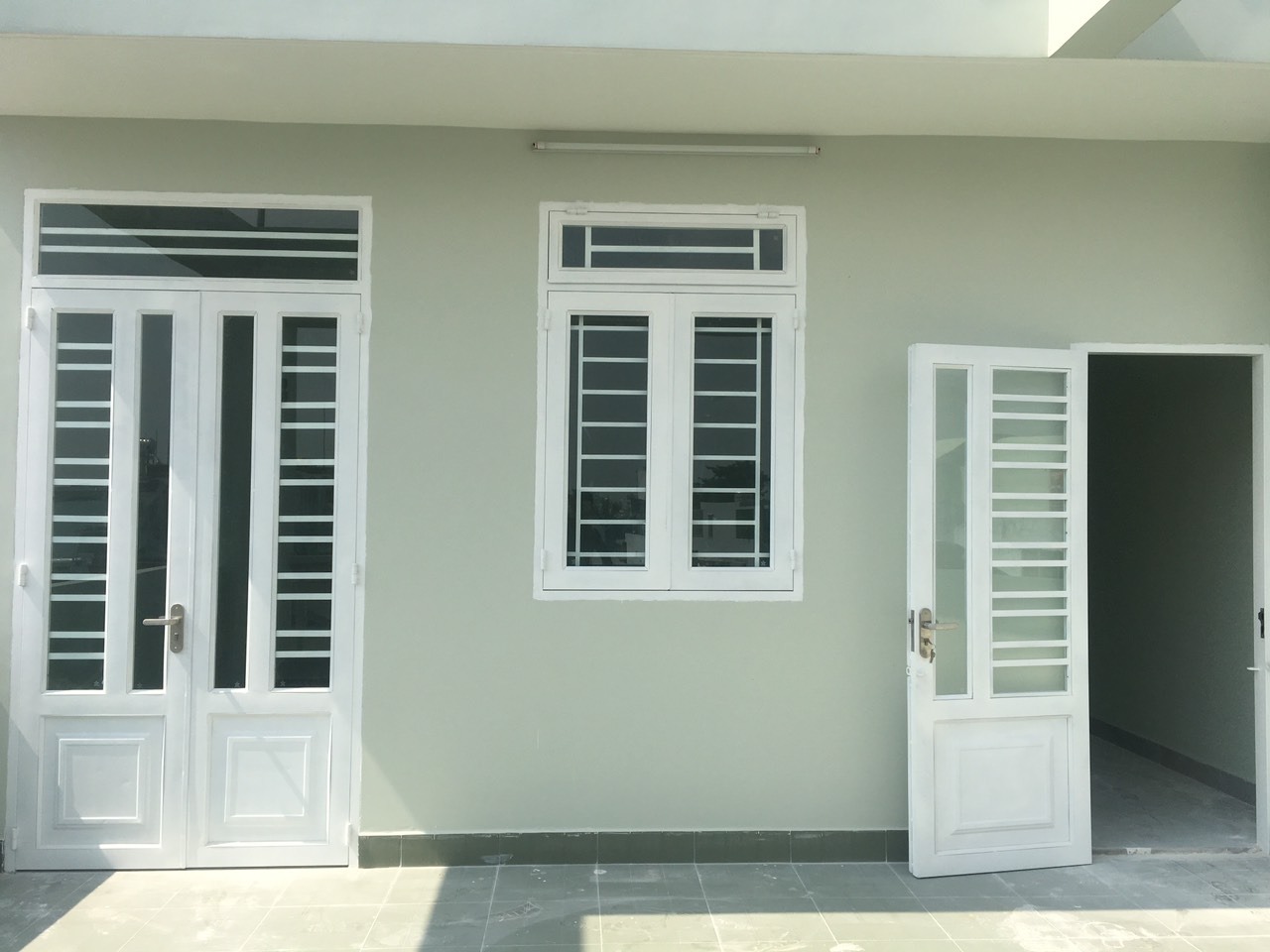 Cửa và cửa sổ trắng trên tường sơn xanh nhạt, ánh sáng ban ngày chiếu qua, tạo không gian thoáng đãng.