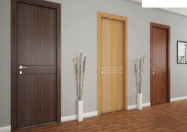 cua-phong-ngu-go-cong-nghiep Ba cánh cửa gỗ màu sắc khác nhau trong nội thất hiện đại, trang trí với bình hoa đơn giản trên sàn gỗ.