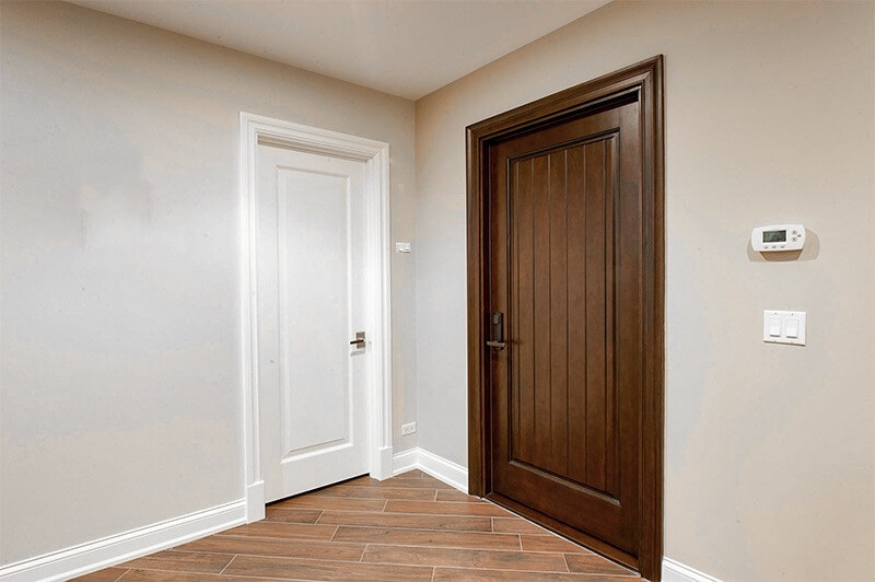 Hai cánh cửa, một trắng và một gỗ nâu, trong lối vào với tường màu xám và sàn gỗ.