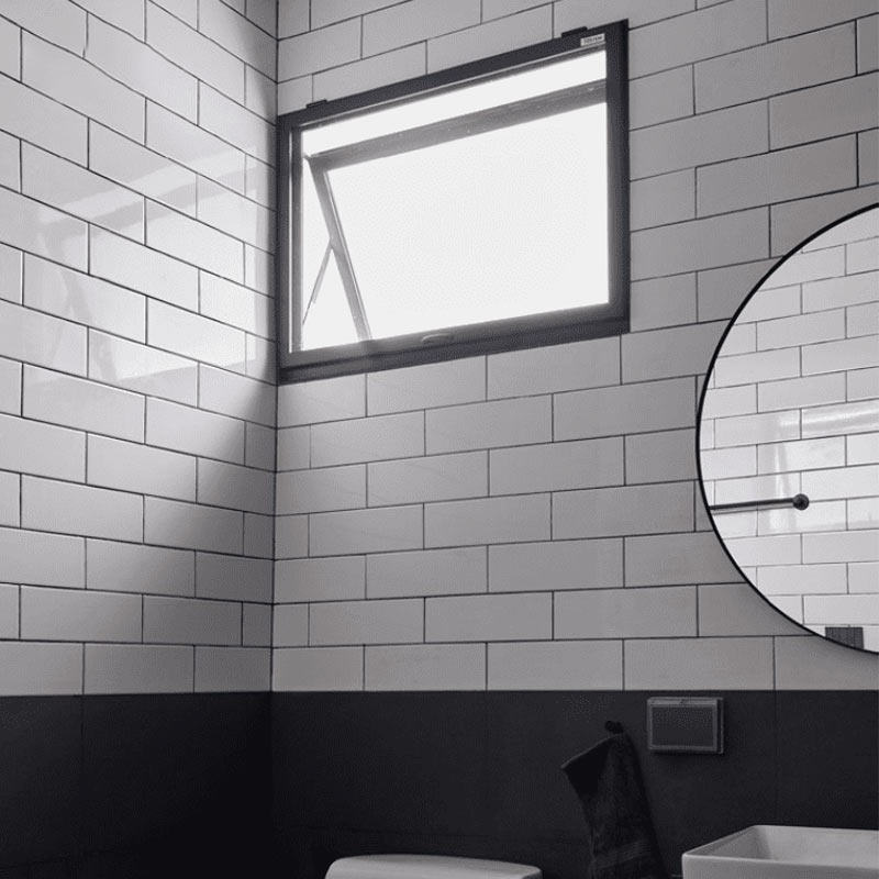 Phòng tắm lát gạch trắng, cửa sổ mở đón sáng, gương tròn và bồn rửa, thiết kế hiện đại và sạch sẽ.