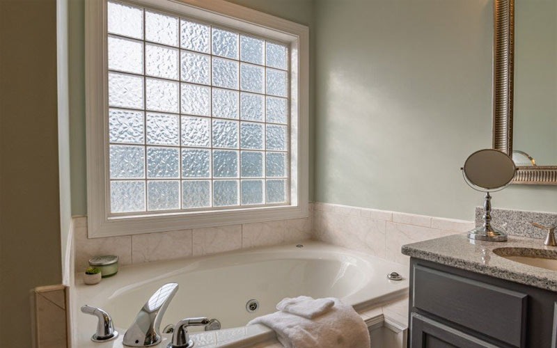 Phòng tắm sáng sủa với bồn tắm lớn, cửa sổ kính mờ và quầy đá granite.