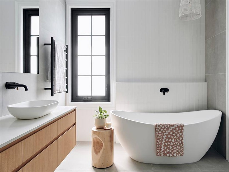 Phòng tắm hiện đại với bồn tắm trắng, chậu rửa và cửa sổ lớn, phong cách tối giản.