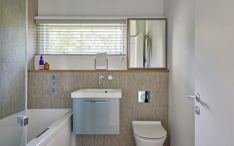 Phòng tắm hiện đại với bồn tắm, bồn rửa và gương, cửa sổ có rèm, tường màu sáng và ánh sáng tự nhiên.