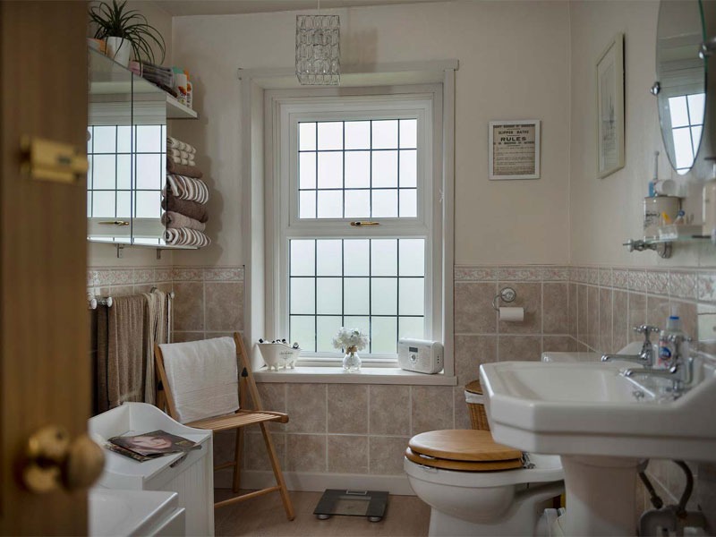 Phòng tắm hiện đại với cửa sổ lớn, bồn rửa, và tủ gương. Nội thất sáng, gọn gàng và thoáng đãng.