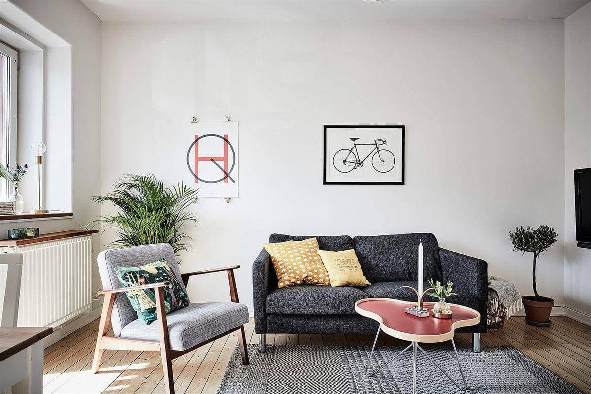 Phòng khách hiện đại, trang trí ghế sofa, bàn trà, và cây xanh; tranh xe đạp treo tường trắng.