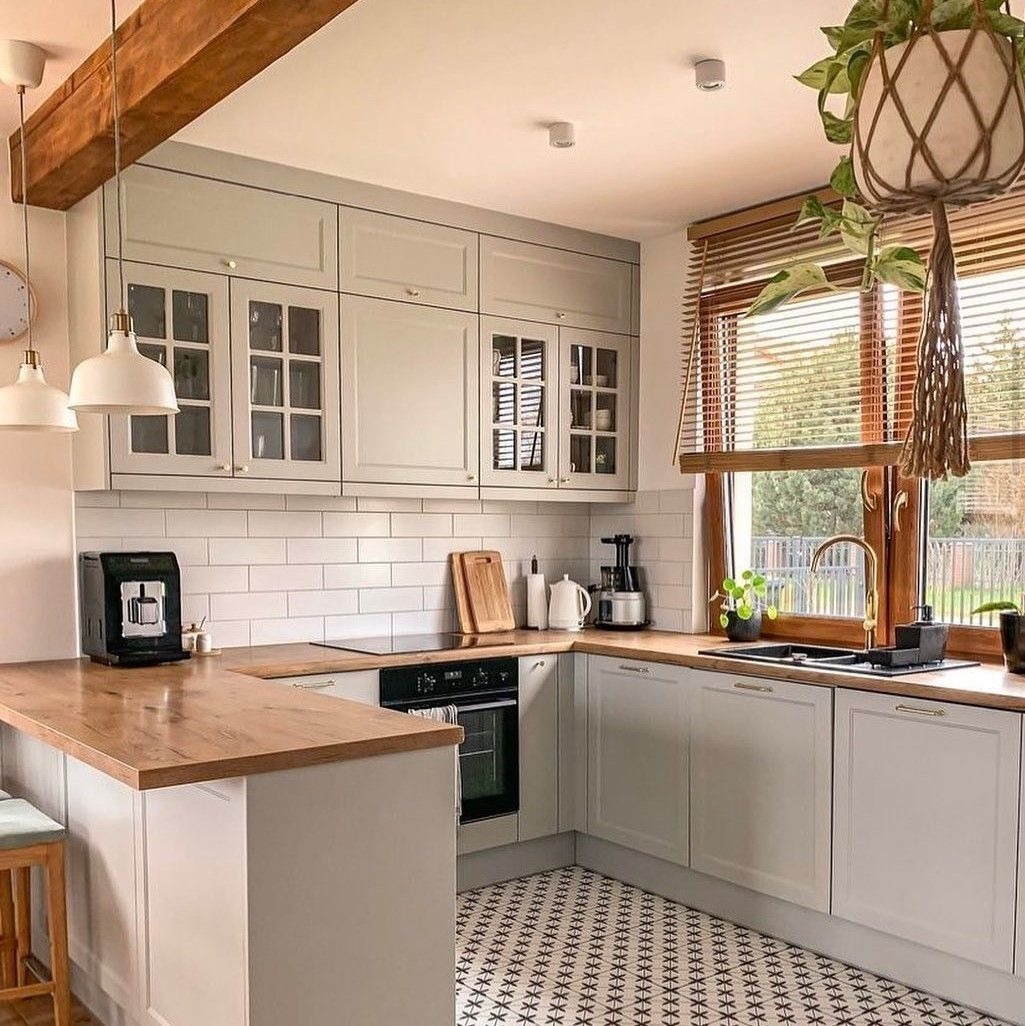 dam-bao-thong-thoang-va-tien-dung Nhà bếp hiện đại với tủ màu trắng, bàn gỗ và cây xanh treo. Cửa sổ lớn với rèm và ánh sáng tự nhiên.