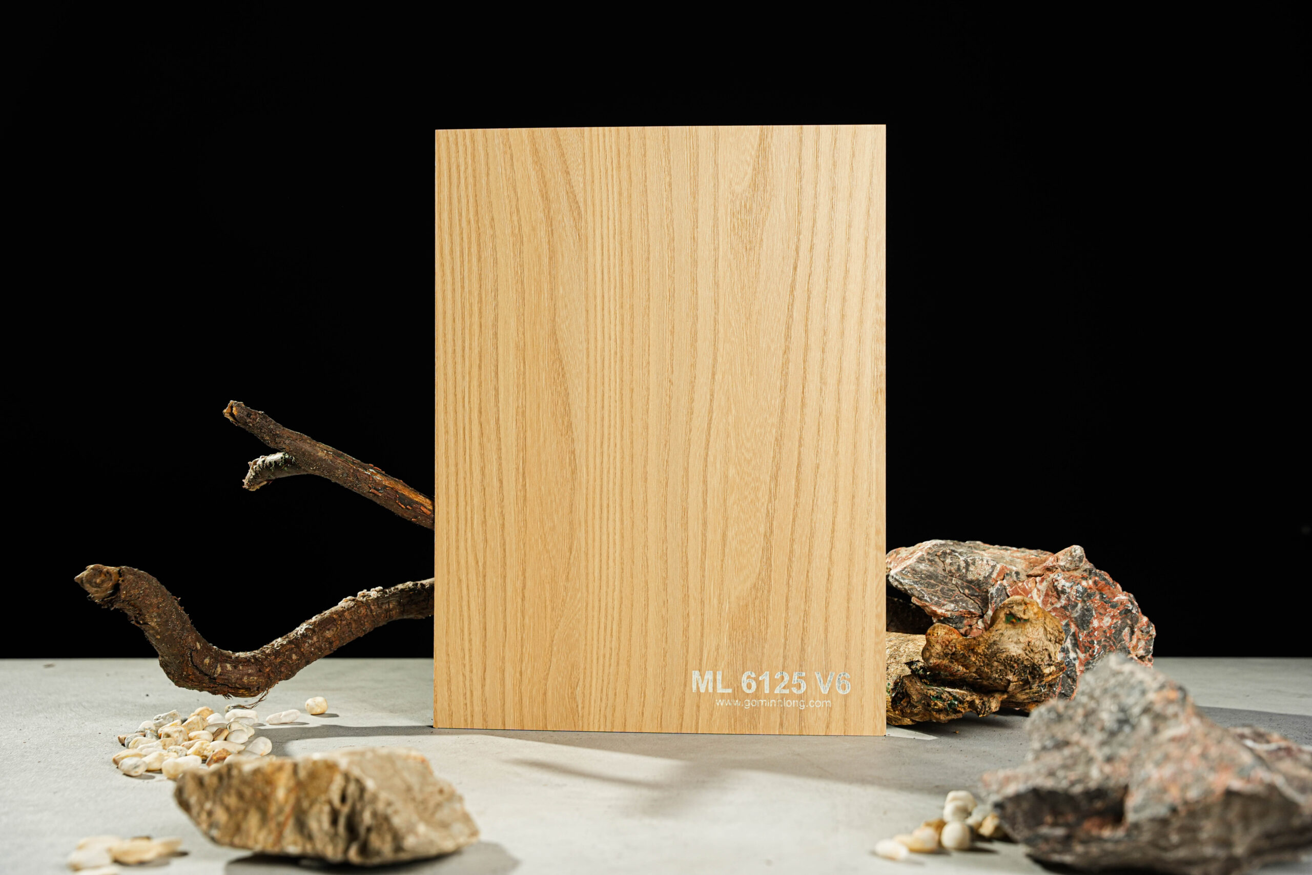 Tấm gỗ vân sáng ML 6125 V6 đứng trên nền đá và nhành cây, tạo khung cảnh nền tối.