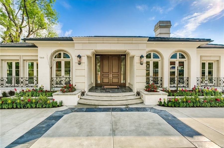 Ngôi nhà kiến trúc cổ điển với cửa gỗ lớn, sân trước rộng và sân vườn trồng hoa.