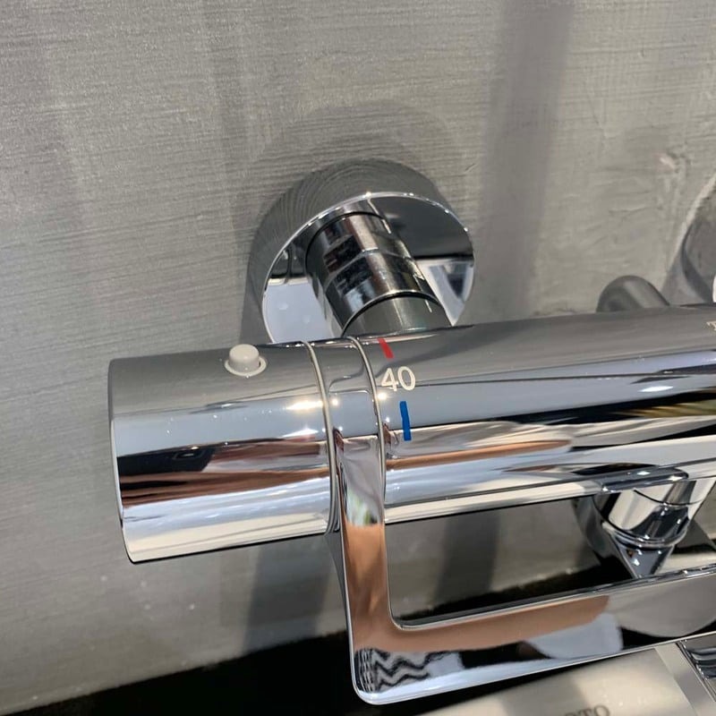 Vòi sen nhiệt độ, mặt số điều chỉnh, màu bạc sáng bóng, nhiệt độ chỉ 40 độ C, lắp trên tường màu xám.