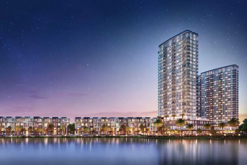 Tòa nhà cao tầng cạnh bờ sông lung linh dưới bầu trời đêm đầy sao, ánh sáng phản chiếu trên mặt nước.