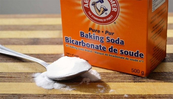 dung-baking-soda Hộp baking soda và thìa bột trên bàn gỗ, thương hiệu Arm & Hammer, dùng trong nấu nướng và làm sạch.