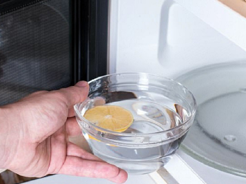 dung-giam-trang Tay cầm tô nước với lát chanh đưa vào lò vi sóng, làm sạch lò bằng cách hấp hơi nước chanh.