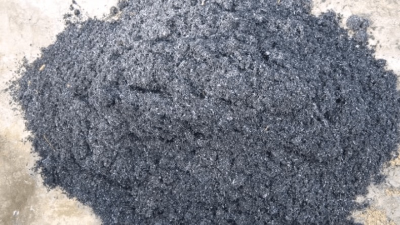 Đống giấy vụn tái chế màu xám đen trên nền bê tông.