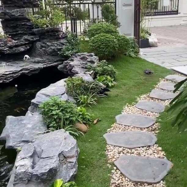 Lối đi lát đá bên hồ cá và cây xanh trong vườn nhỏ, tạo khung cảnh thư giãn tự nhiên.