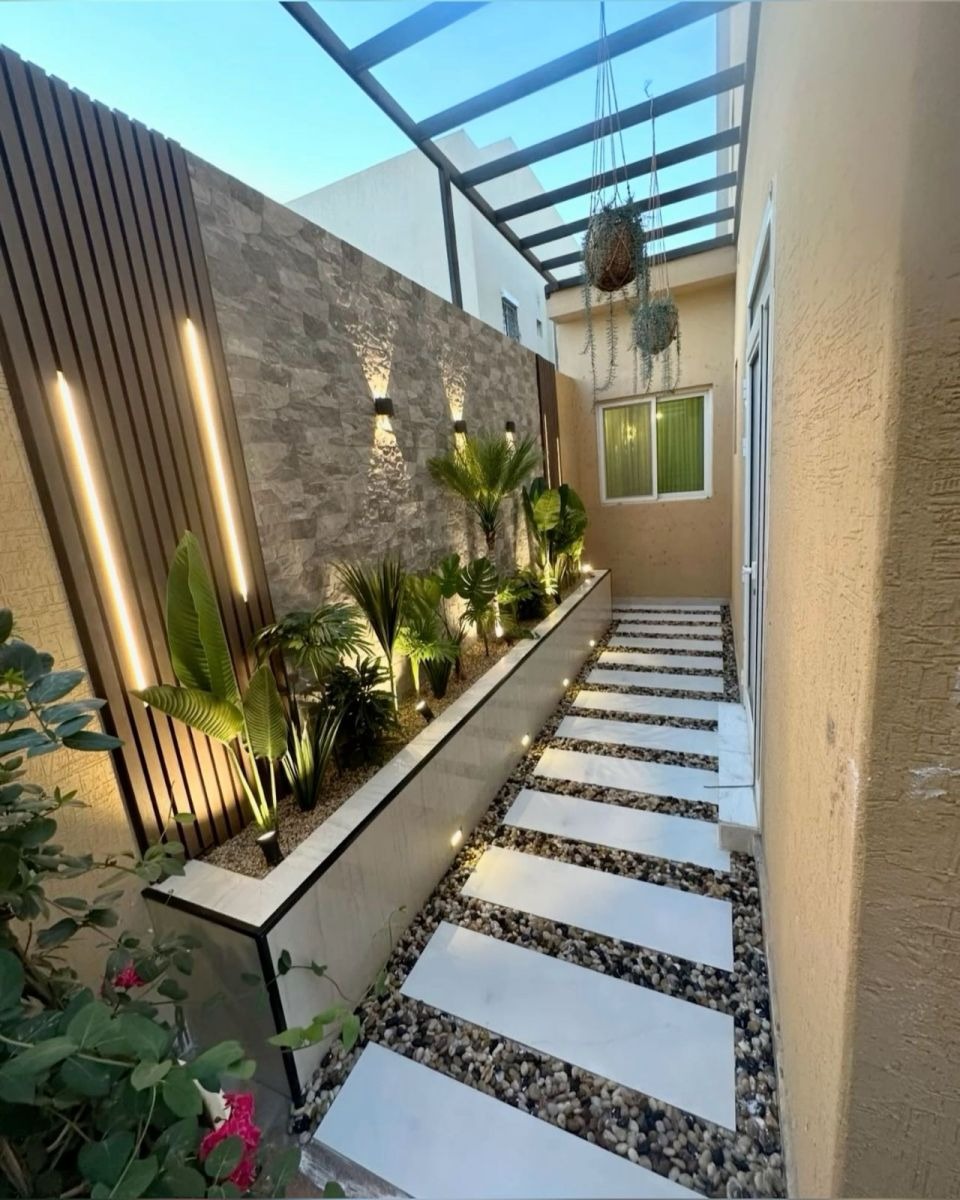 Lối đi sân vườn nhỏ, lát đá, trang trí cây xanh, ánh sáng đèn LED, tường gạch trang trí, không gian thư giãn hiện đại.