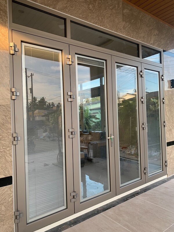 Cửa nhôm kính hiện đại màu xám, ánh sáng xuyên qua, phản chiếu khung cảnh bên ngoài.