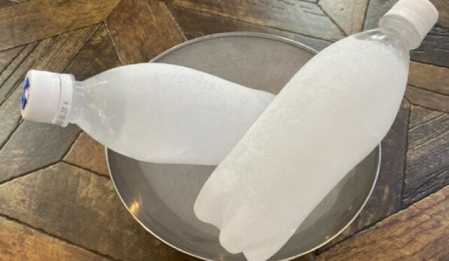 Hai chai nước đông lạnh trong đĩa kim loại trên bàn gỗ, chuẩn bị chủ động làm mát.