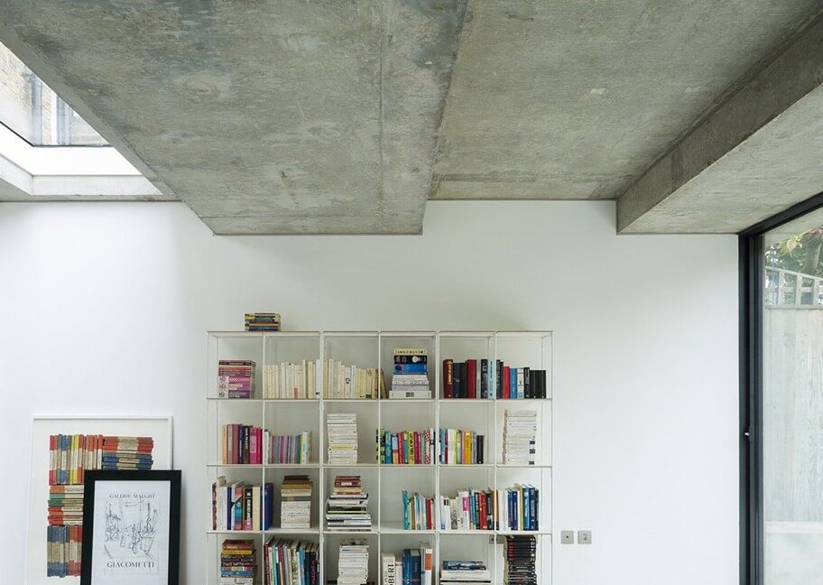 Kệ sách hiện đại trong phòng khách với trần bê tông và cửa sổ lớn, tạo không gian sáng và thoáng đãng.