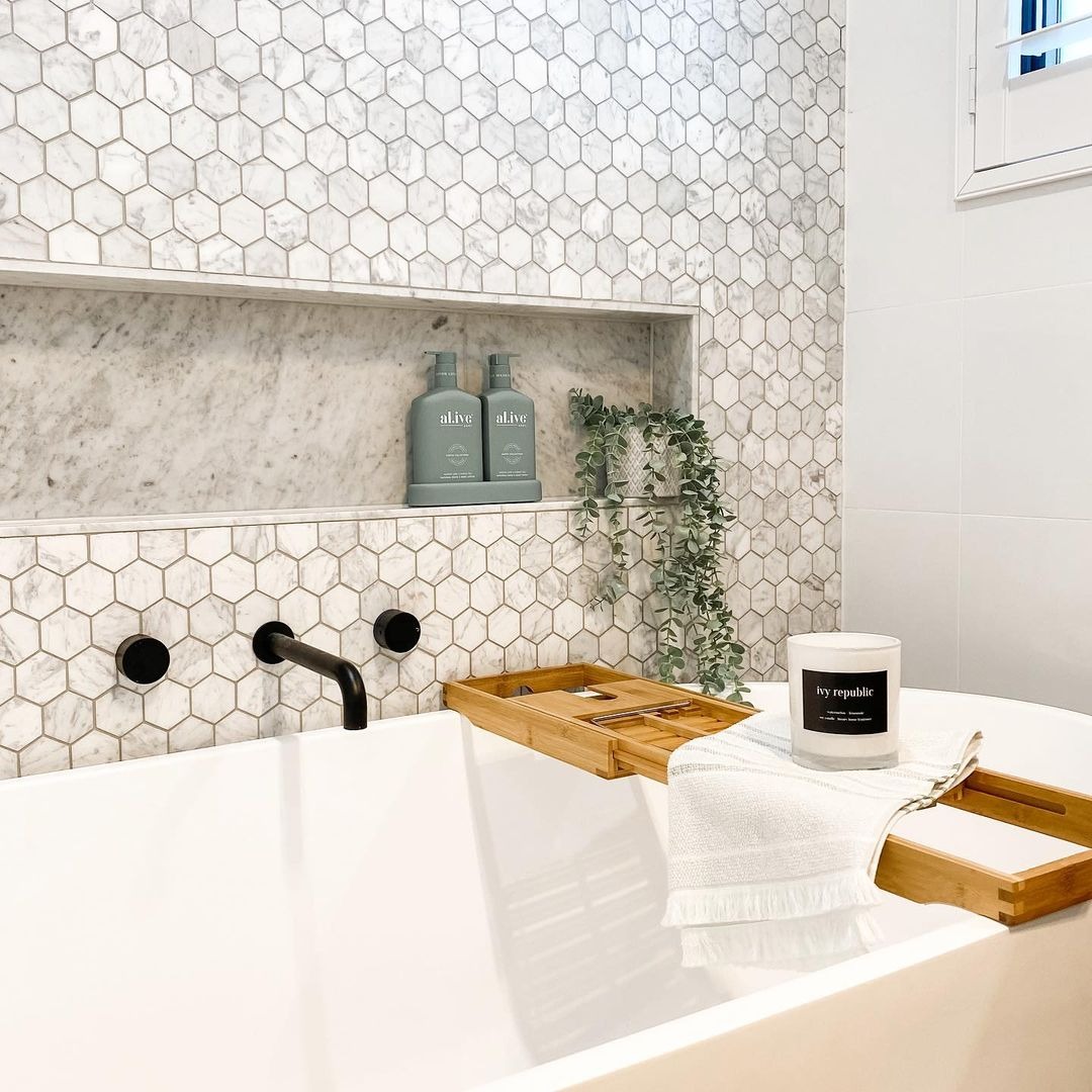 Bồn tắm với gạch lát tổ ong, vòi nước đen, và khay gỗ kèm nến thơm, tạo không gian thư giãn hiện đại.