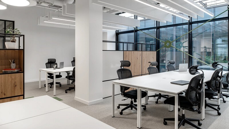 Văn phòng hiện đại với bàn ghế làm việc, ánh sáng tự nhiên, không gian mở và nội thất tối giản.