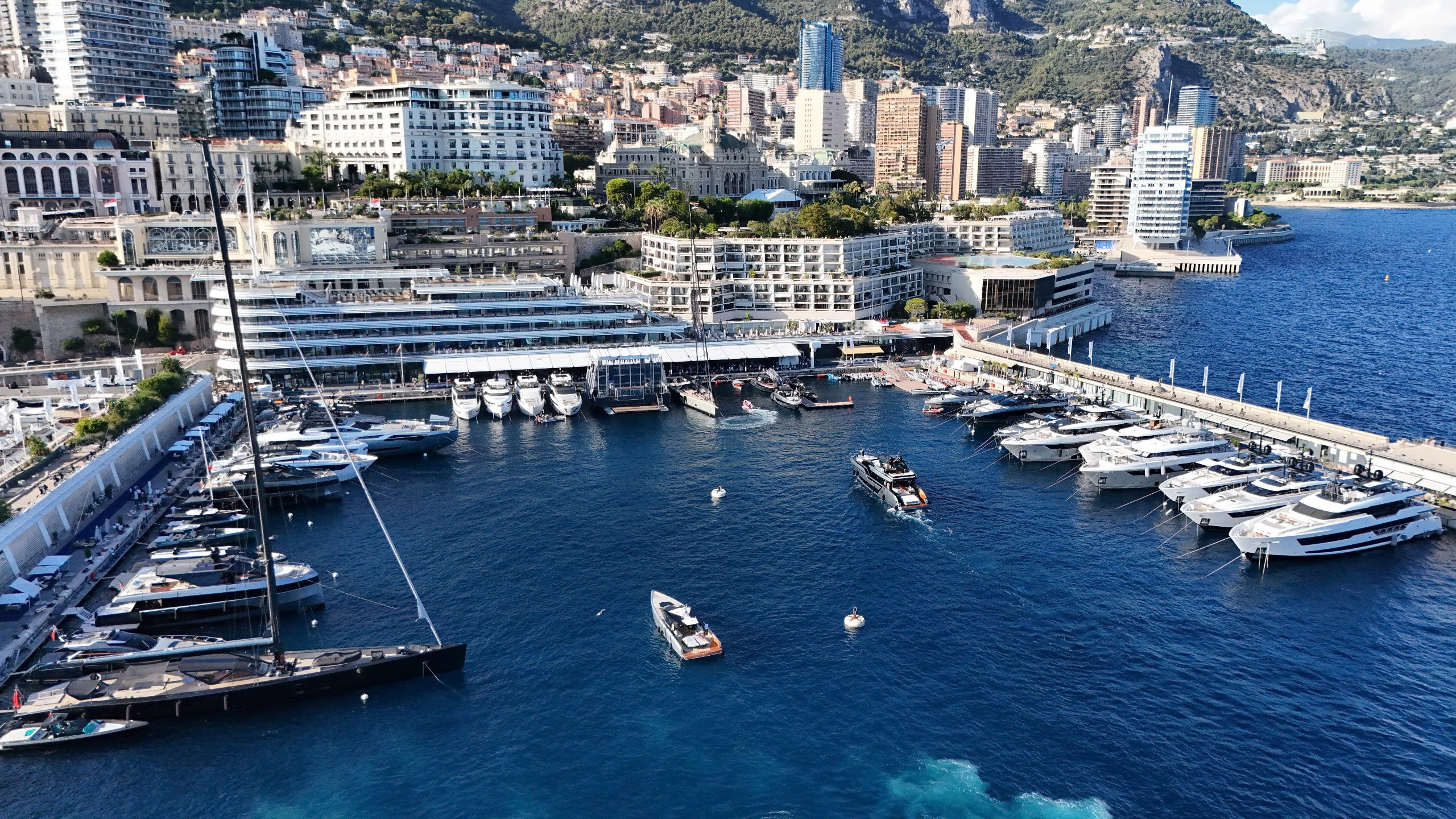 Bến cảng Monaco sầm uất với du thuyền sang trọng và tòa nhà cao tầng ven núi, nhìn từ trên cao.