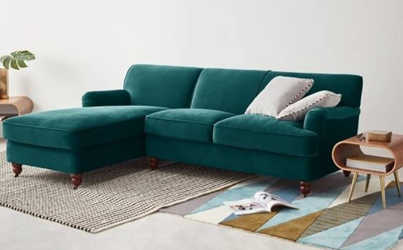 ghe-sofa-lam-bang-nhung Sofa góc màu xanh lục, cùng gối trang trí trên thảm sọc, tạo không gian phòng khách hiện đại và thoải mái.