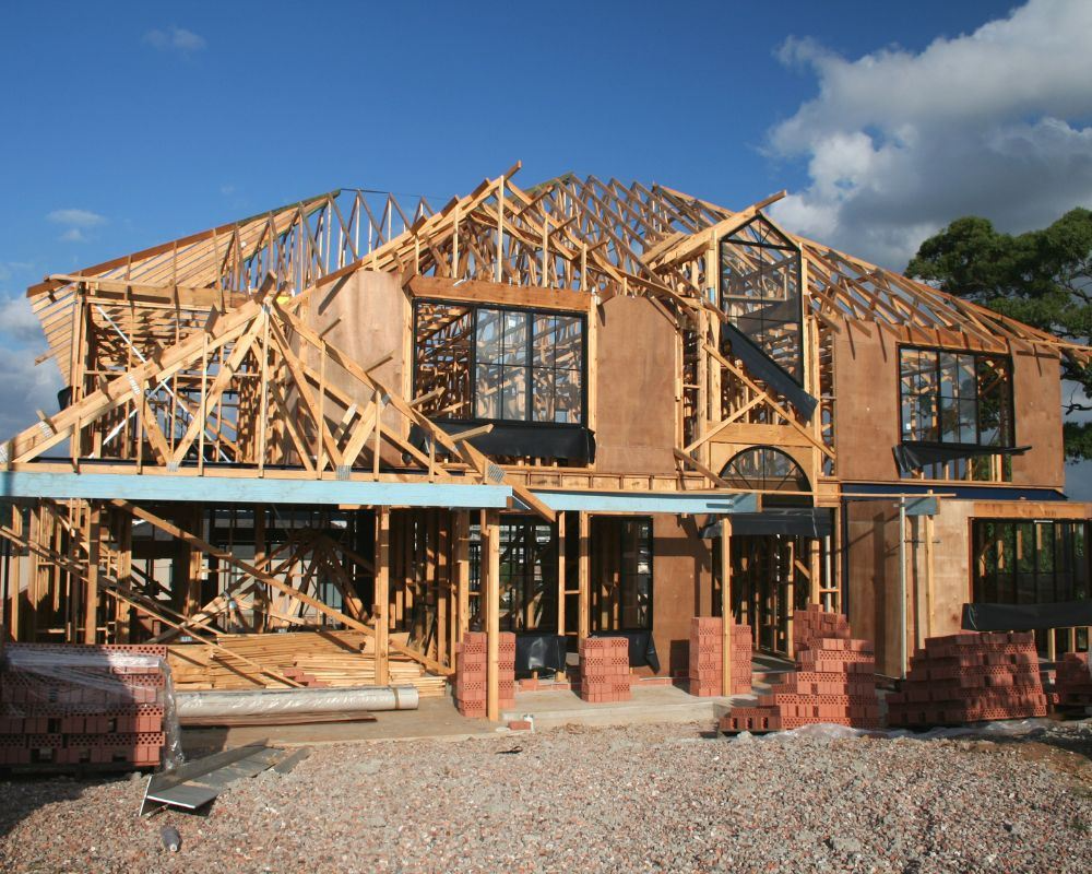 Nhà đang xây với khung gỗ và gạch xếp chồng, bối cảnh trời xanh và mây trắng.