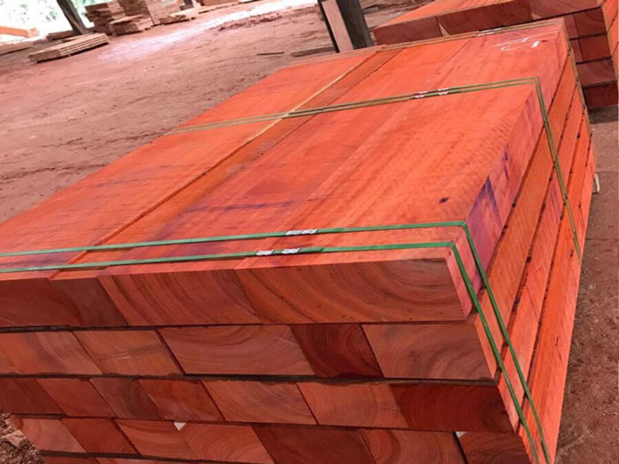 Các thanh gỗ đỏ xếp chồng gọn gàng trong xưởng, chuẩn bị vận chuyển.