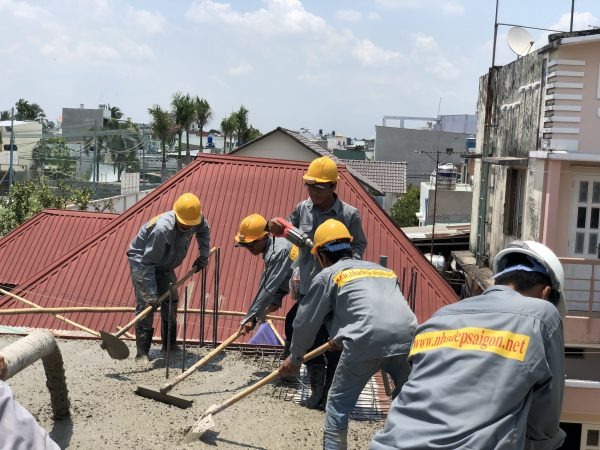 Các công nhân xây dựng đội mũ bảo hộ, làm việc trên mái nhà với dụng cụ xây dựng dưới bầu trời nắng.