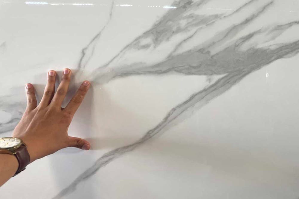 Tay chạm vào bề mặt đá hoa cương trắng vân xám, thể hiện chất lượng và độ bền của vật liệu xây dựng cao cấp.