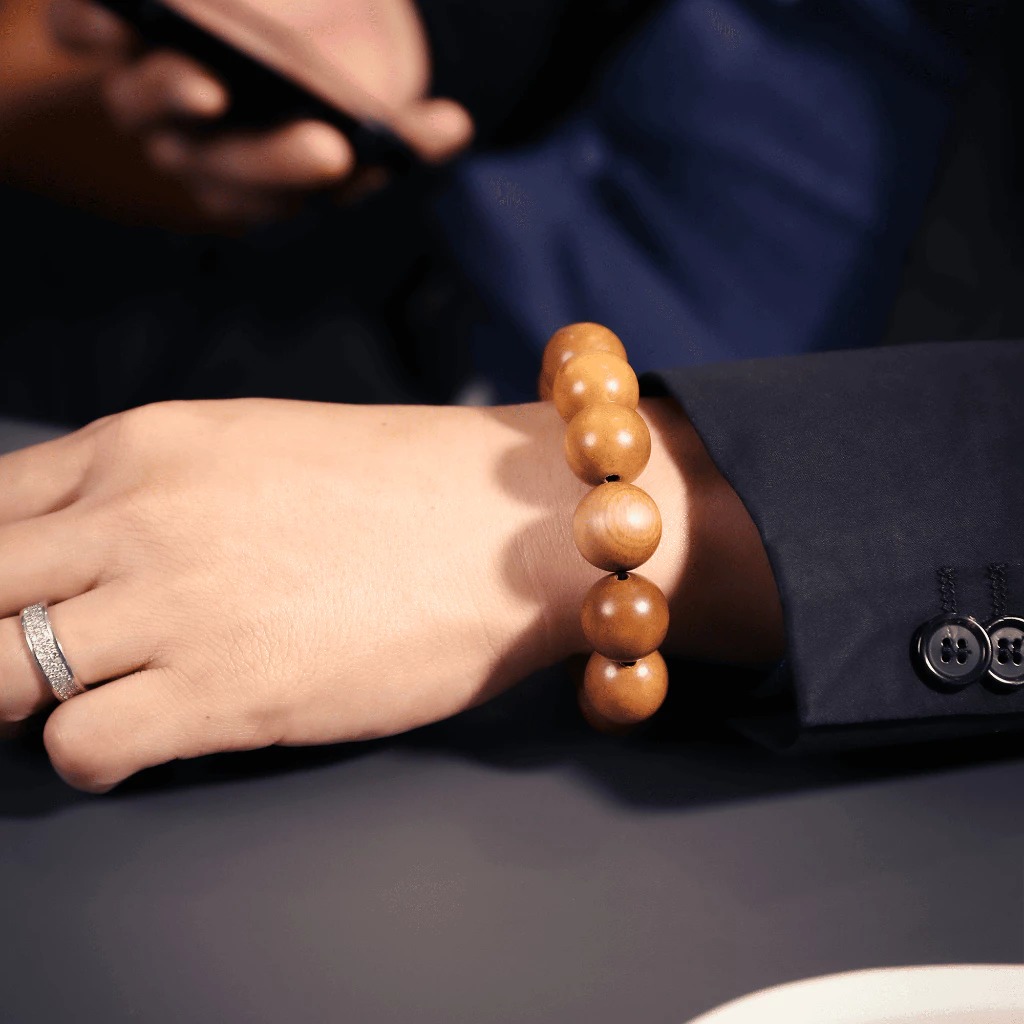 Tay đeo vòng tay gỗ, áo vest xanh đậm, nhẫn bạc, sử dụng điện thoại di động, phong cách lịch lãm.