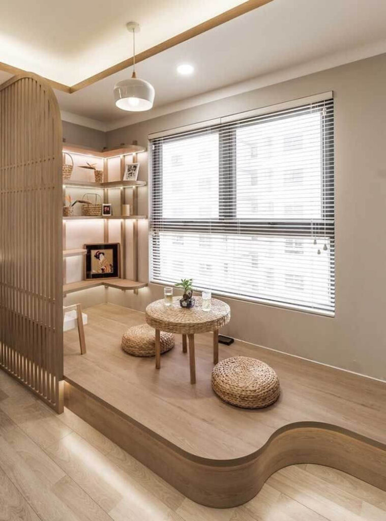 Phòng khách nhỏ gọn với bàn trà gỗ, đệm ngồi mây, ánh sáng tự nhiên từ cửa sổ lớn và kệ sách trang trí tối giản.