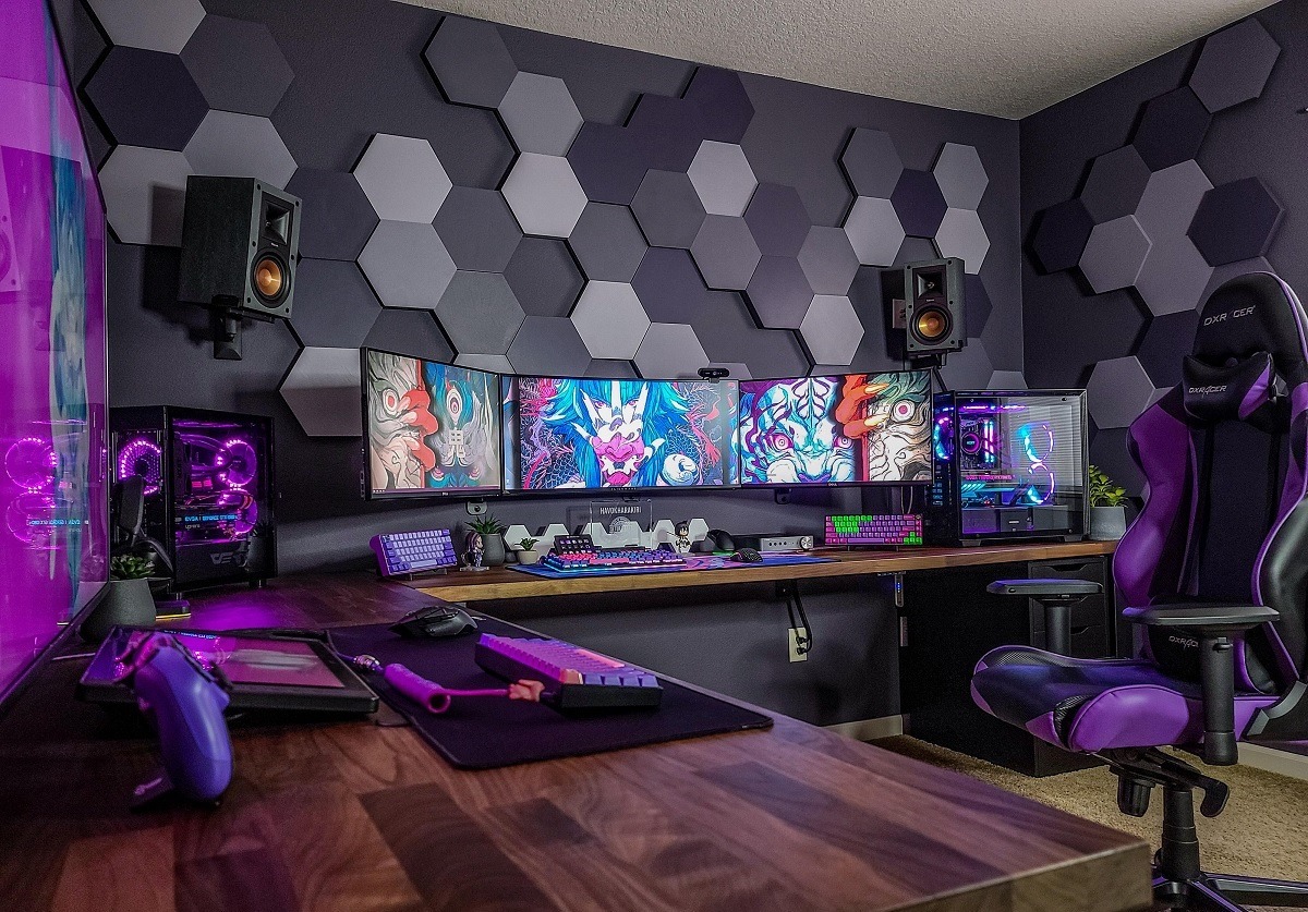 Bàn máy tính hiện đại với ba màn hình và ghế chơi game DXRacer trong phòng tường trang trí tổ ong.
